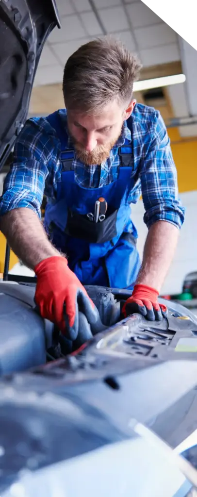 Een monteur met rode handschoenen en een blauw geruit overhemd, geconcentreerd bezig met het repareren van een automotor in een helder verlichte garage, die concentratie en vakmanschap uitstraalt.