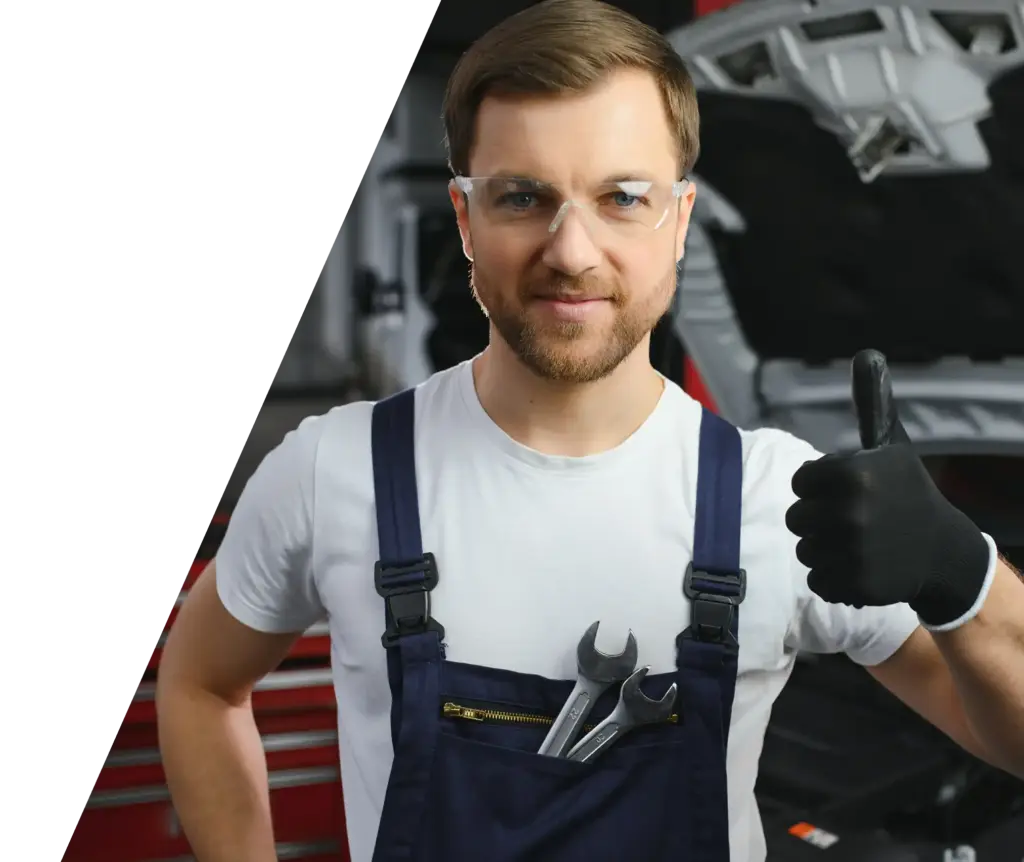 Professionele automonteur met veiligheidsbril die een duim omhoog steekt in een moderne autoreparatiewerkplaats.